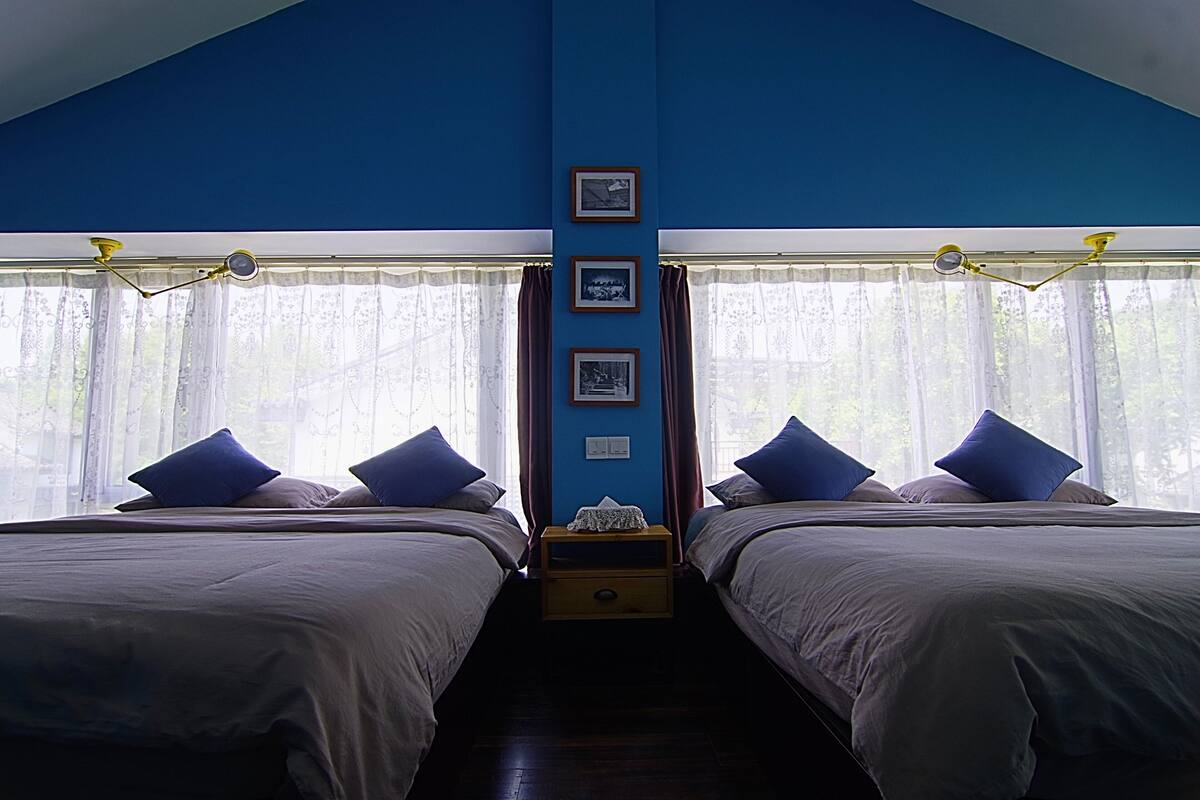 A bedroom with two beds, a nightstand, and a window with curtains.