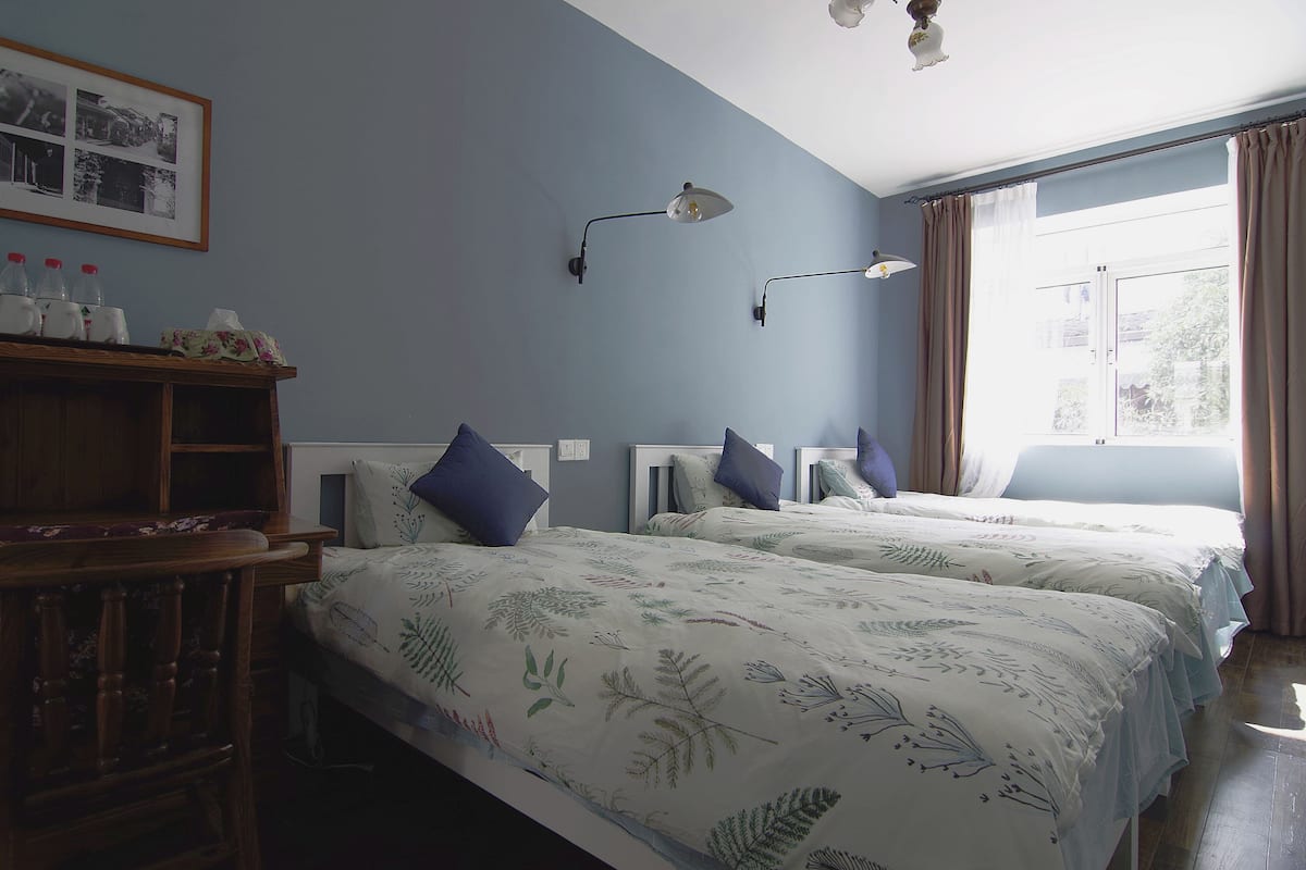 A room with two beds, a wooden desk, and a wall-mounted shelf with bottles.