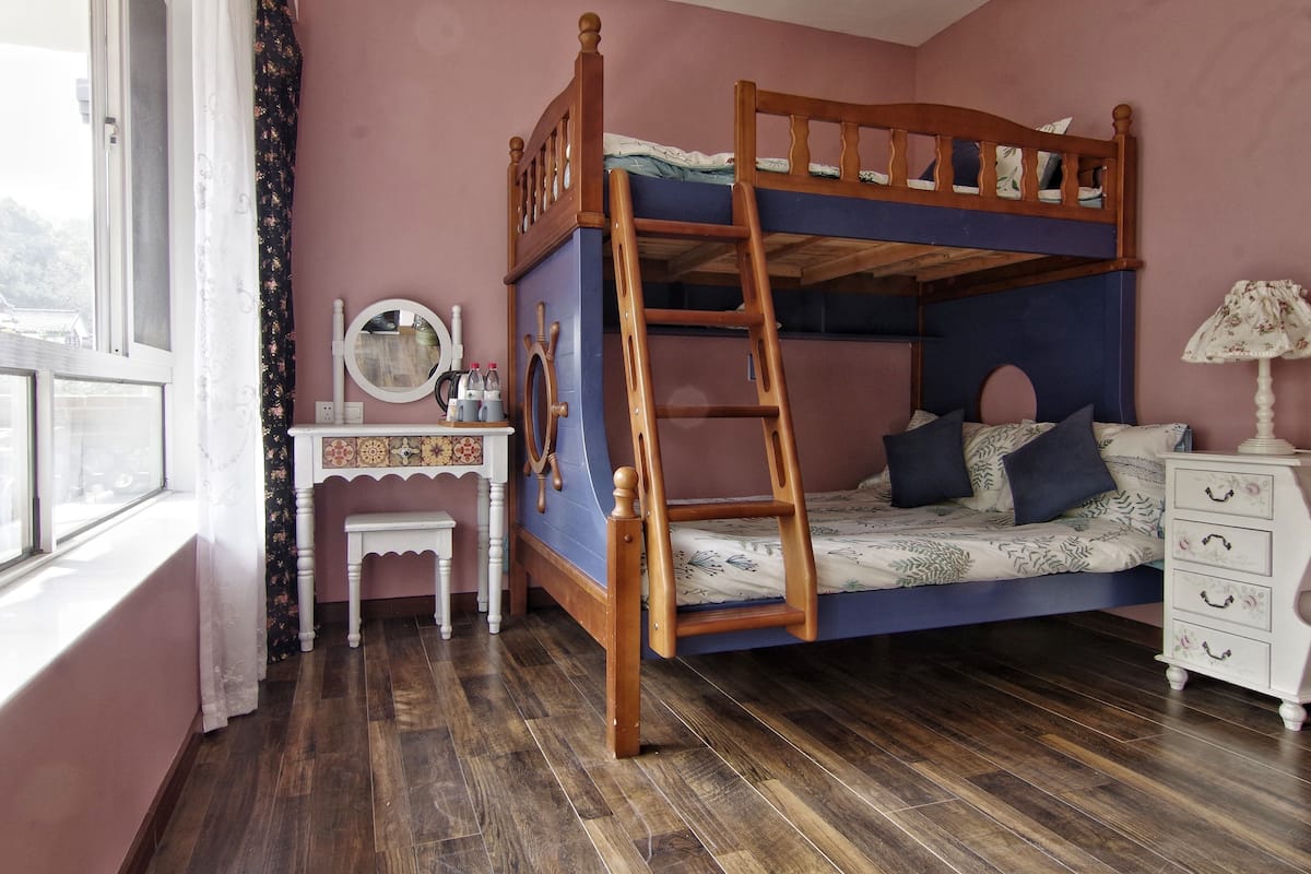 A bunk bed with a wooden ladder, a small white desk with a mirror, and a dresser with drawers.