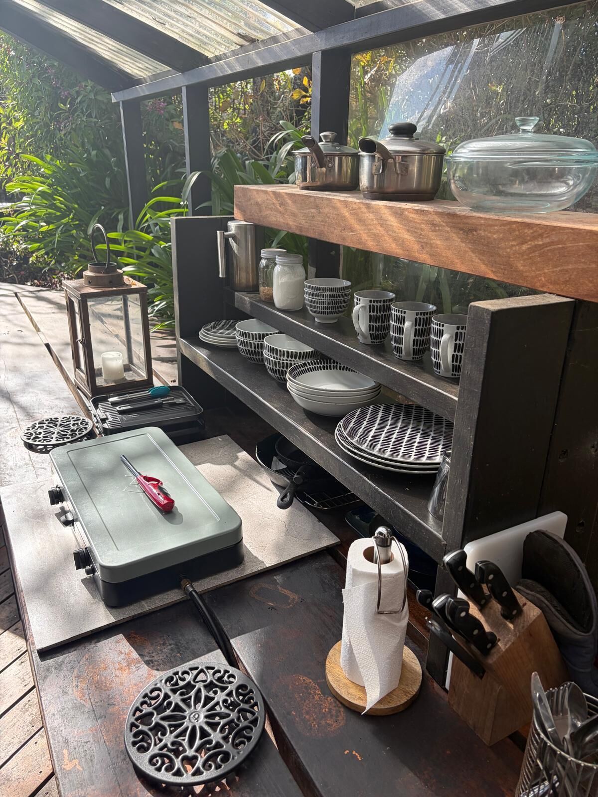Un coin cuisine équipé d’une cuisinière intégrée, d’une étagère en bois où sont rangés les ustensiles de cuisine, et d’une variété d’accessoires de cuisine.