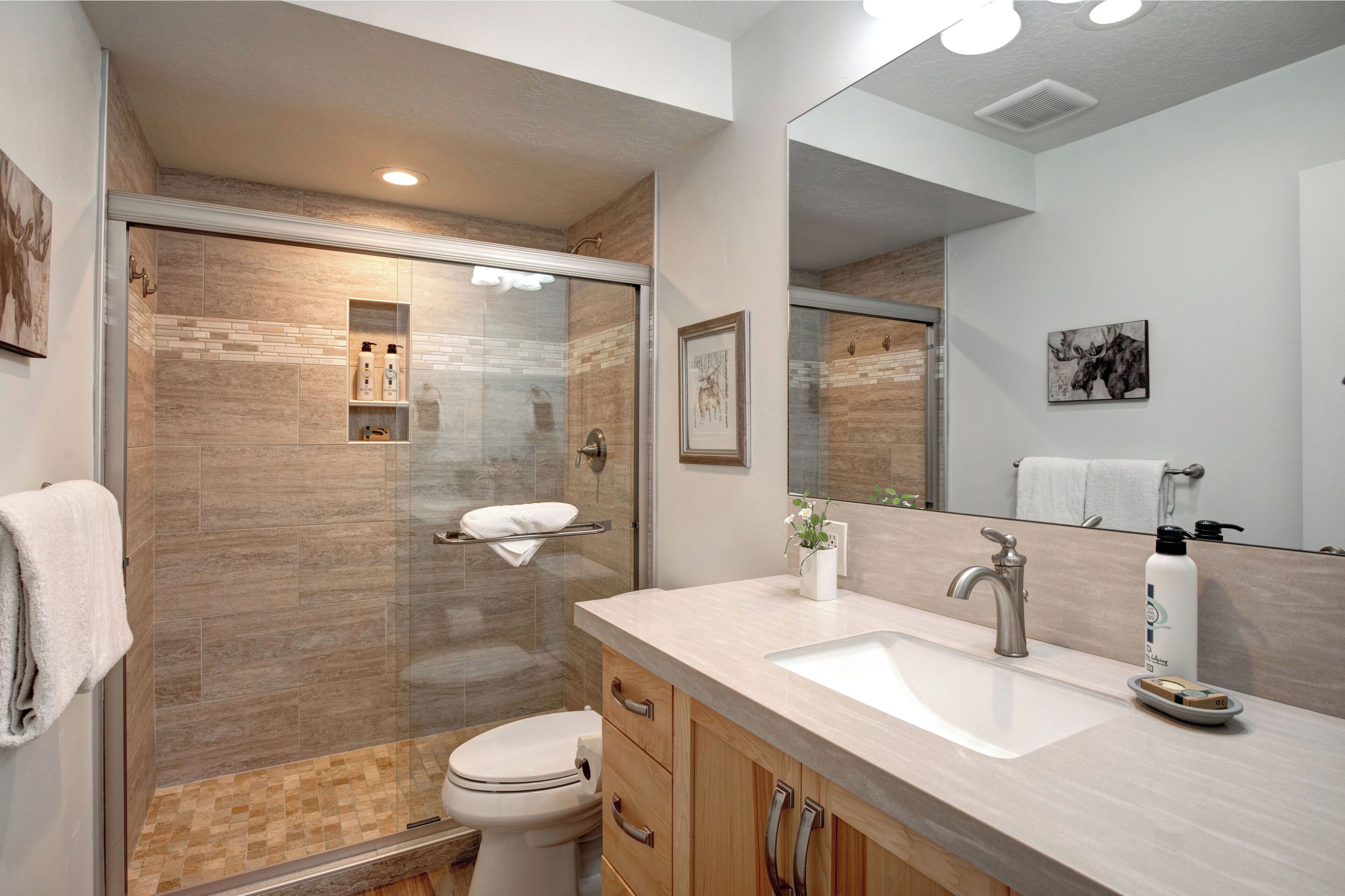 A modern bathroom with a glass-enclosed shower, a white sink, and wooden cabinets.