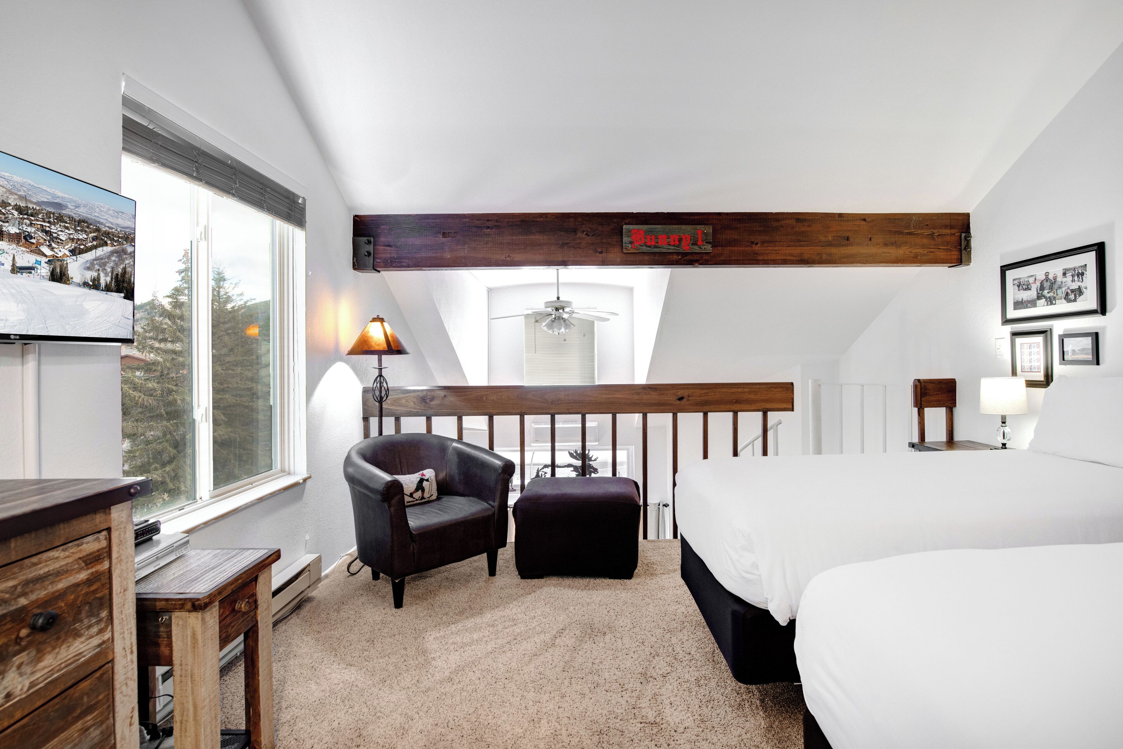 A bedroom with a large bed, a chair, a small table, a TV, and a window with a view of a snowy landscape.