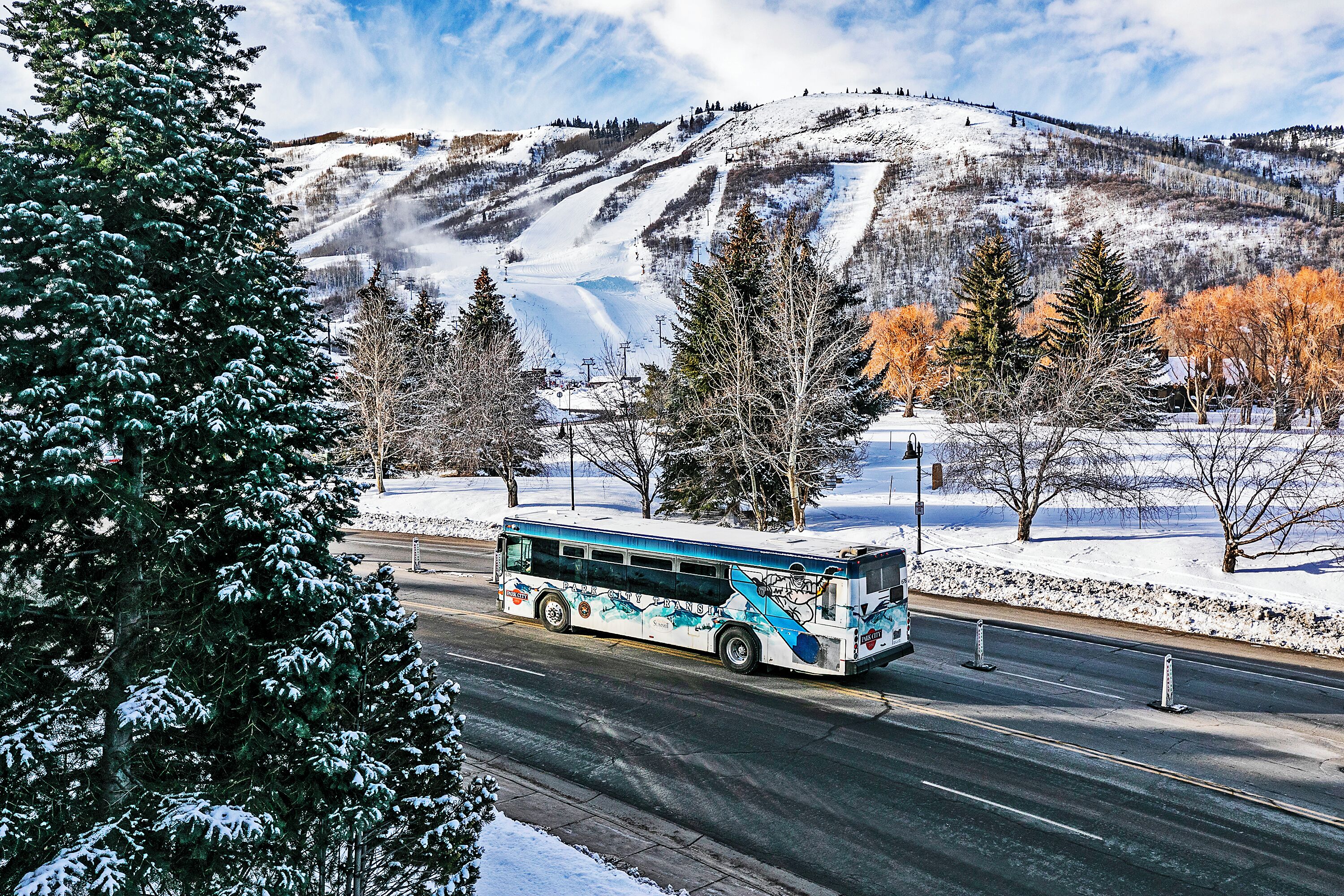 A bus on a snow-covered road with a mountainous backdrop.