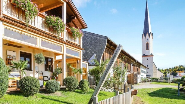 Een traditioneel houten gebouw met een balkon, een kerk met een hoge spits en een verzorgde tuin.