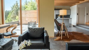 Una sala moderna con sofá, una zona de comedor con sillas, una cocina con lámpara y vistas amplias a través de grandes ventanales.