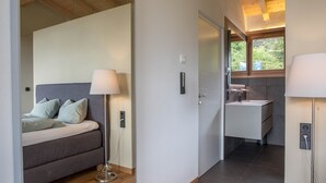 Un dormitorio moderno con cama, lámpara de noche y vistas a un baño con lavabo y ventana.