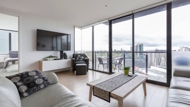 A modern living room with a large TV, a sofa, a coffee table, and a balcony with a city view. - Melbourne and Southbank Gem with 3 bedrooms (Southbank)