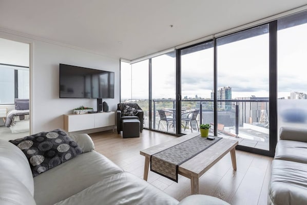 Relax in this stylish living room with a large flat-screen TV, comfortable sofa, and city views from the balcony.