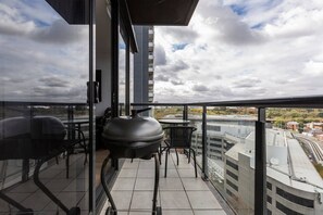 Enjoy the urban view from this balcony with a glass railing, black grill, and seating for two.