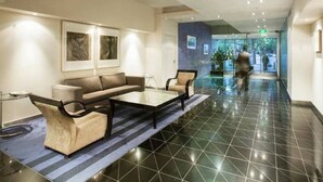 A hotel lobby with a reception desk, seating area, and a glass wall offering a view of the outdoors. - Melbourne and Southbank Gem with 3 bedrooms (Southbank)