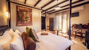 A hotel room with a large bed, a desk, a chair, a small table, and a wall-mounted TV. - Paroraia boutique rooms (Sintiki)