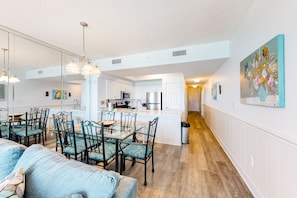 Open-plan living space with a dining area and kitchen featuring a glass-top table and contemporary appliances.