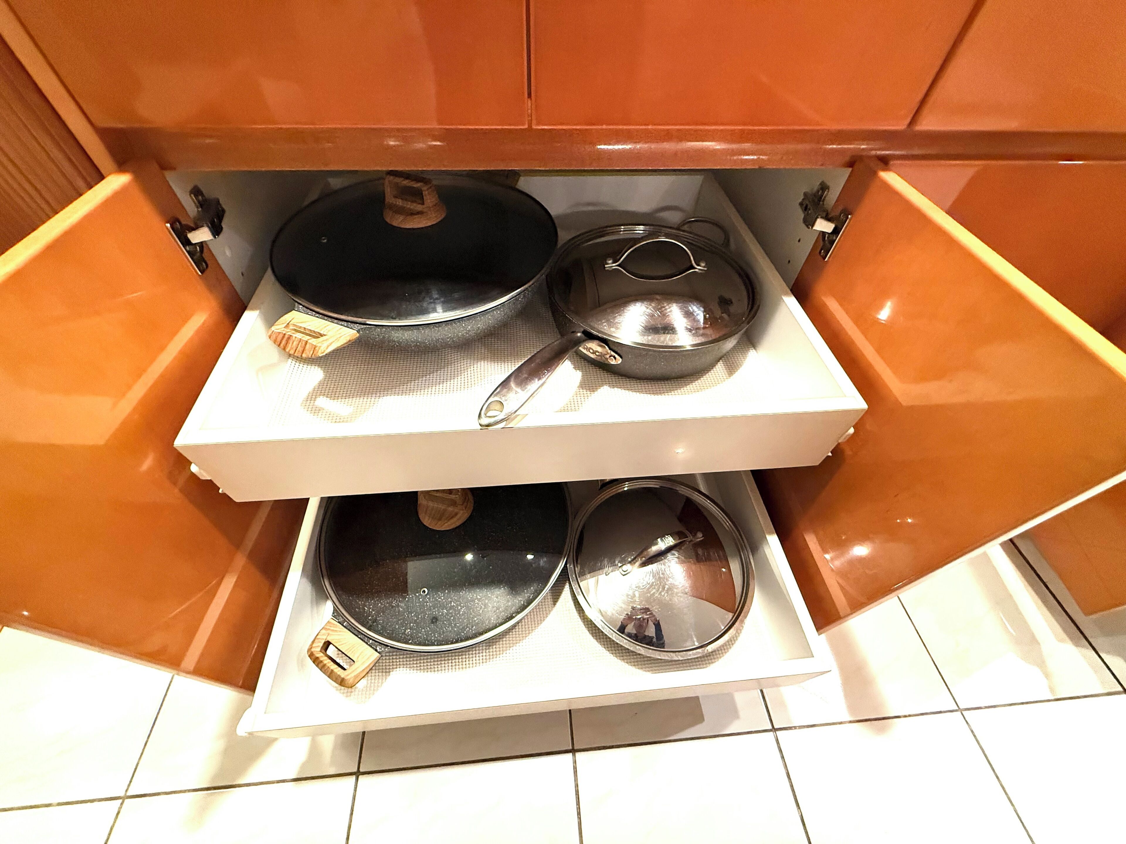 A kitchen cabinet with two shelves, each holding a pot and a pan.