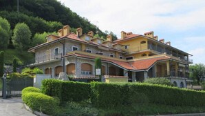 A large, multi-story building with a stone facade and terracotta roof tiles, surrounded by lush greenery and a hillside. - il balcone sul lago (Magreglio)