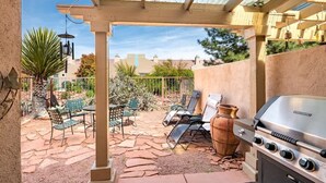 Un patio al aire libre con una parrilla, sillas y una pérgola.