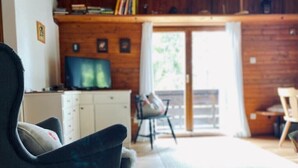 Ein gemütliches Wohnzimmer mit einem dunklen Sessel, einem Fernseher und einem Essbereich aus Holz.