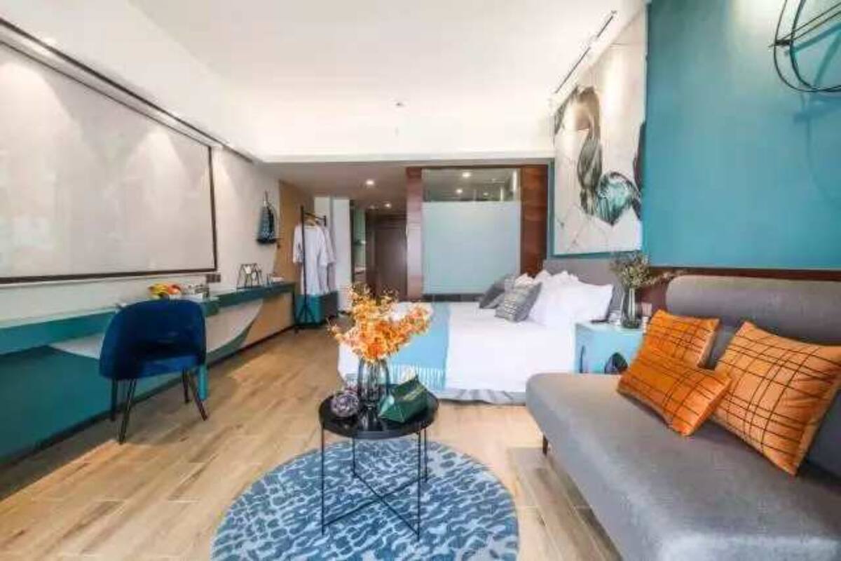 Ett modernt hotellrum med en säng, en soffa, ett litet bord med en vas med blommor och en blå, mönstrad matta.