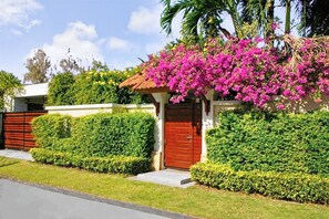 Una casa residencial con puerta roja, setos bien cuidados y un jardín en la azotea con flores rosas.
