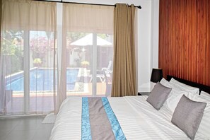 A hotel room with a bed, curtains, a view of the outdoors, and a wooden wall. - Busaba Villa 7 - 3 Bedroom - Pool (Tambon Nong Kae)
