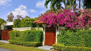 Una casa con puerta roja, rodeada de setos cuidados y un árbol en flor.