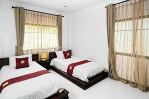 Ein Hotelzimmer mit zwei Betten, beigen Vorhängen, weißer Bettwäsche und einem Holz-Kopfteil.