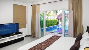 Un dormitorio con cama, televisor sobre un mueble y vista a una piscina exterior.