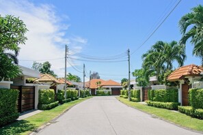 Une rue résidentielle bordée de maisons, avec un ciel dégagé et des lignes électriques.