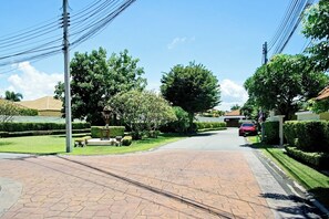 A residential street with a paved walkway, trees, and a parked car.