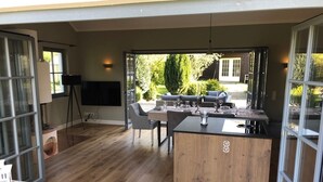 Een moderne keuken met een houten kookeiland, een eethoek met geruit tafelkleed en uitzicht op de tuin door glazen deuren.