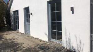 Een wit gebouw met grote ramen en een deur, een verharde inrit en een klein buitengebied met een metalen rooster.