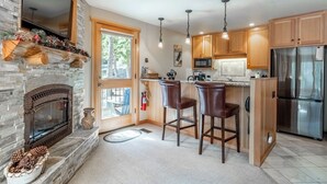 Una cocina con chimenea de piedra, armarios de madera, refrigerador de acero inoxidable y una zona de bar con dos taburetes.
