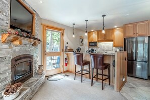 Una cocina con chimenea de piedra, armarios de madera, refrigerador de acero inoxidable y una zona de bar con dos taburetes.