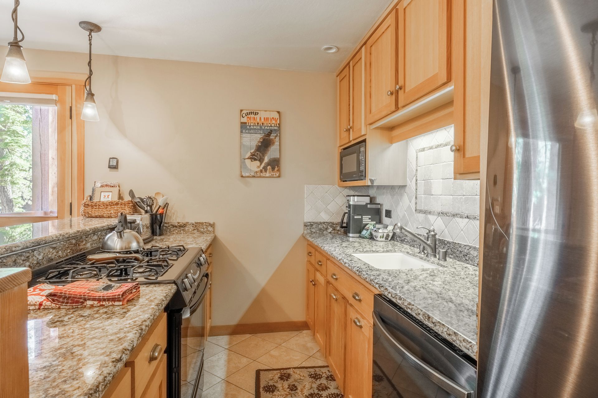 A kitchen with granite countertops, stainless steel appliances, wooden cabinets, and a window with a view of trees.
