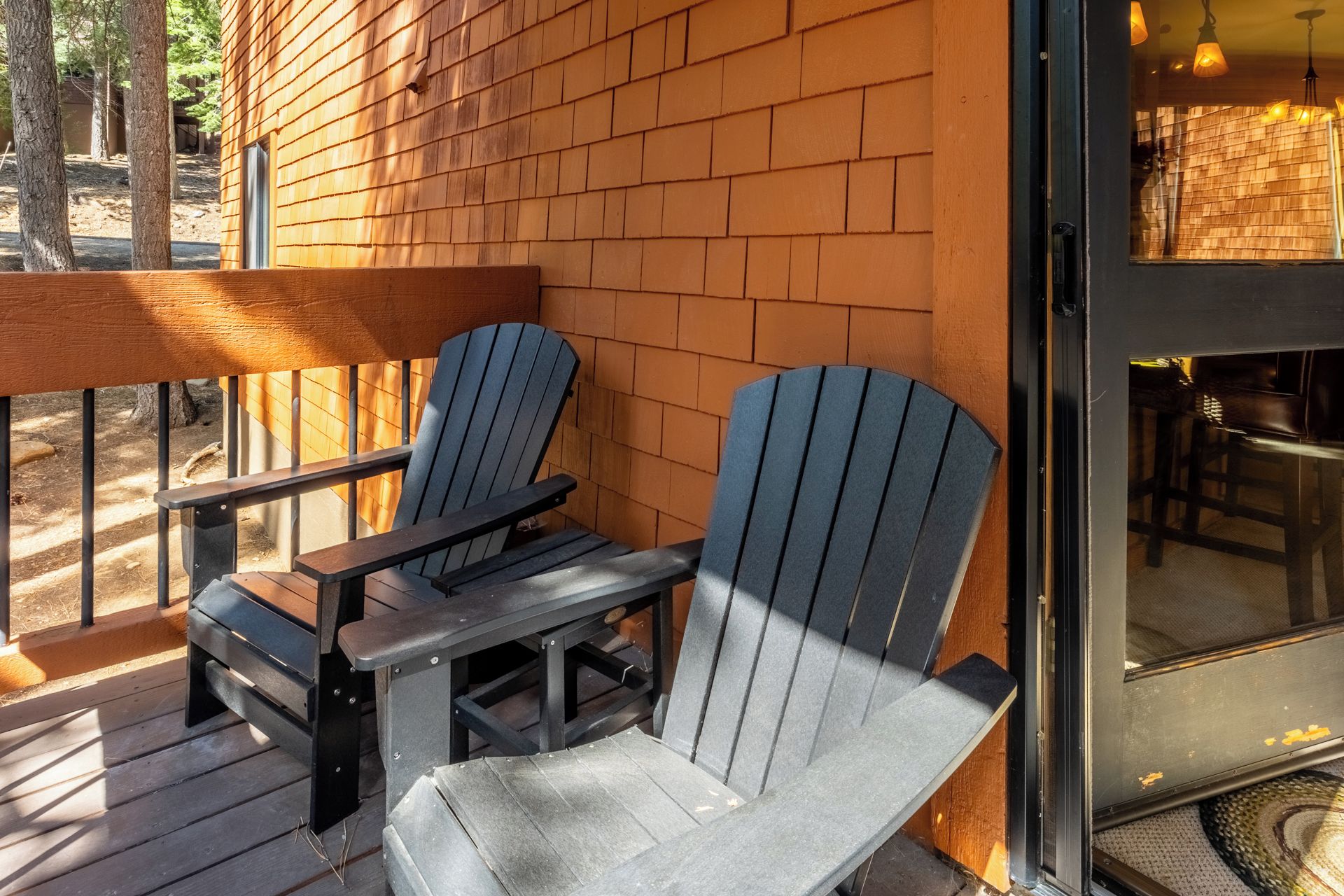Duas cadeiras Adirondack em um deck de madeira com um muro de tijolos ao fundo.