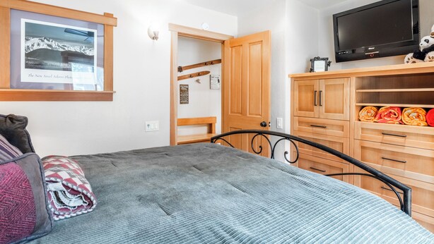 Un dormitorio con una cama, un armario de madera, un televisor y una fotografía enmarcada en la pared.