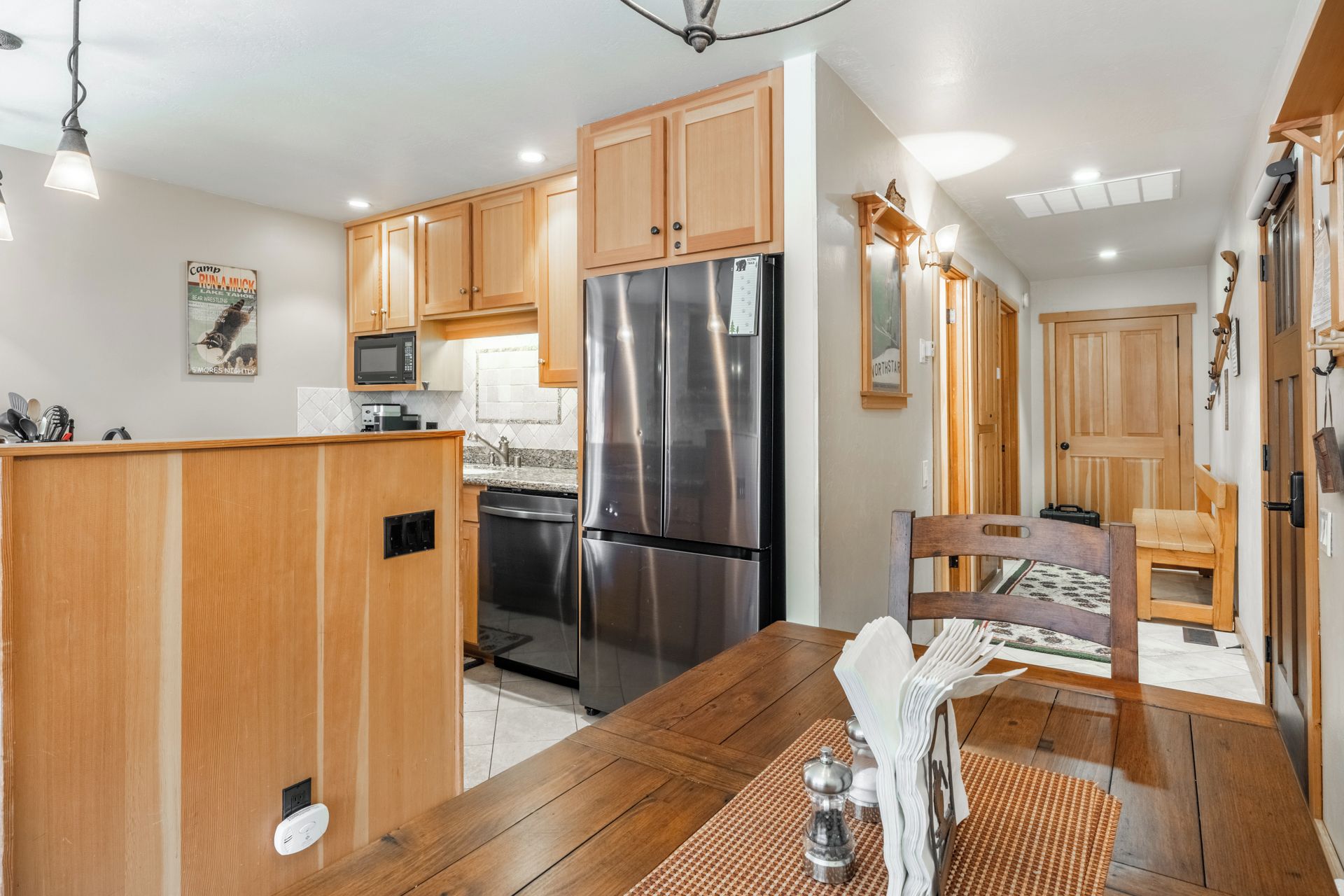A kitchen with wooden cabinets, a stainless steel refrigerator, a microwave, and a dining table with chairs.