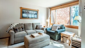 Una sala de estar acogedora con un sofá gris, un sillón azul y una mesa de centro de madera.