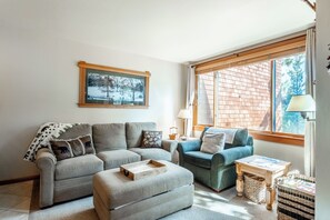 Una sala de estar acogedora con un sofá gris, un sillón azul y una mesa de centro de madera.