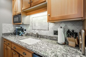 Una cocina con encimeras de granito, armarios de madera, microondas integrado y un lavamanos.