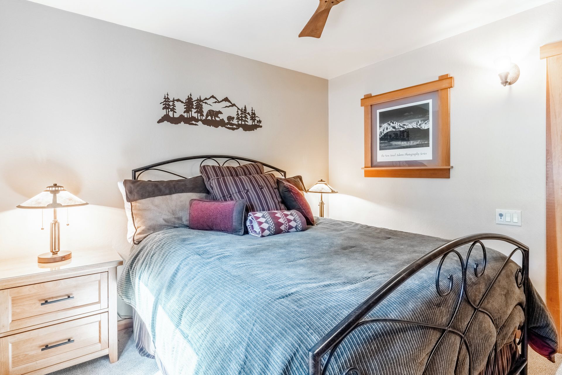 A bedroom with a bed, bedside tables, a wall-mounted picture, and a ceiling fan.