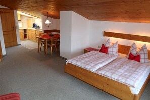 Ein Schlafzimmer mit einem hölzernen Bett, einem Esstisch und einer Küche im Hintergrund.