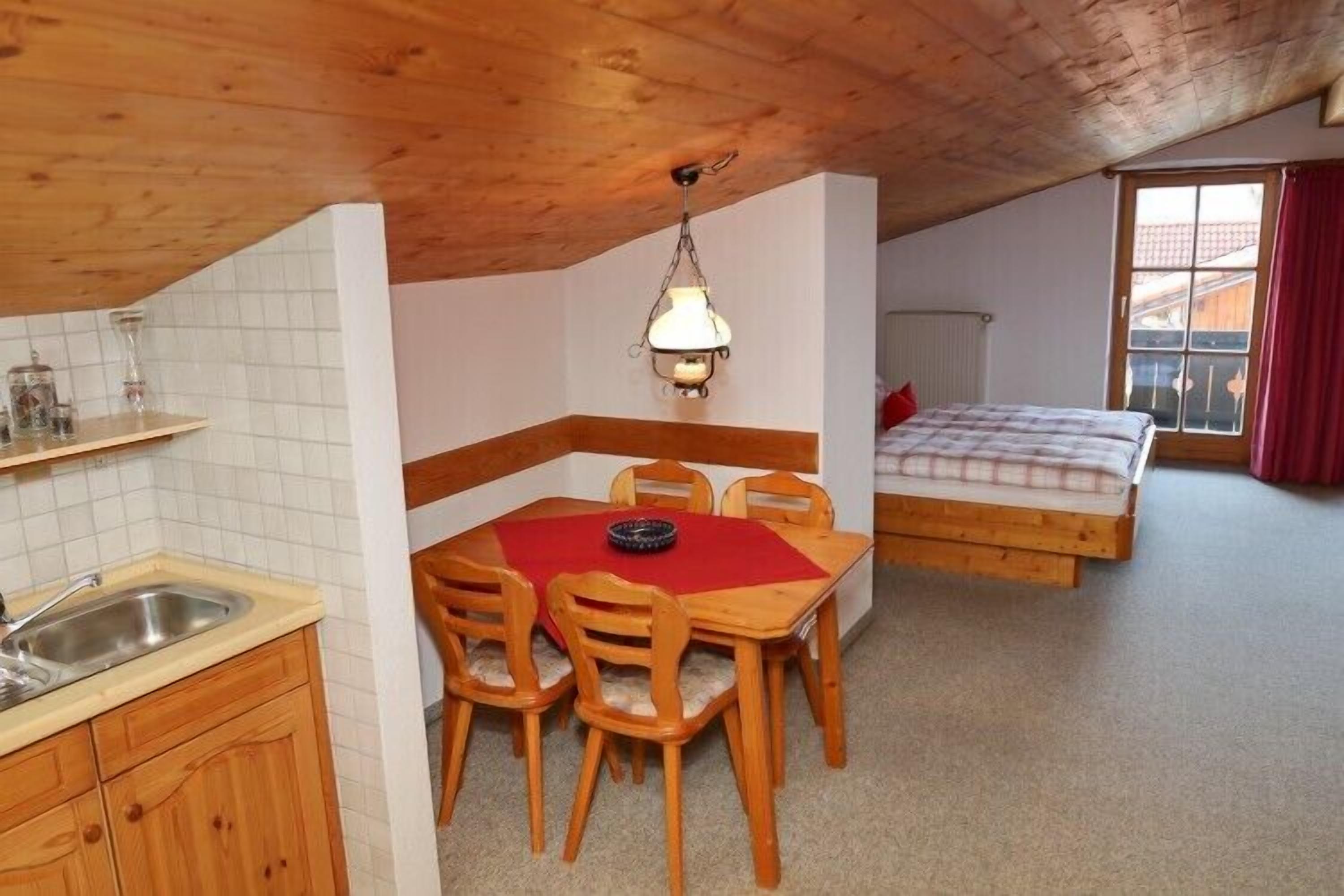Una habitación compacta con área de cocina, una mesa de comedor con sillas, una cama con cortina roja y una ventana con vistas.