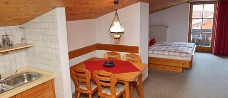 Una habitación compacta con área de cocina, una mesa de comedor con sillas, una cama con cortina roja y una ventana con vistas.