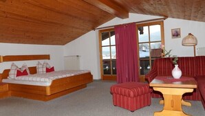 A cozy room with a wooden ceiling, a bed, a sofa, and a table with a vase.