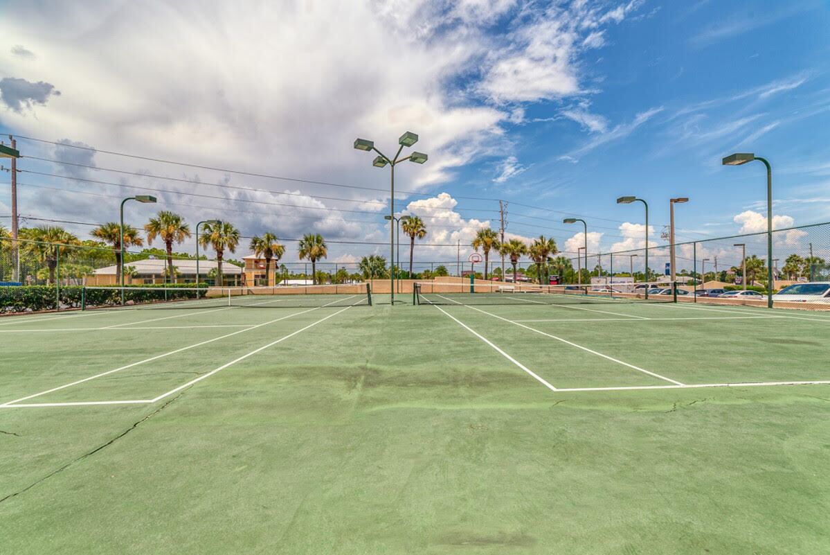 En tennisbana med nät, omgiven av palmer och gatlyktor.