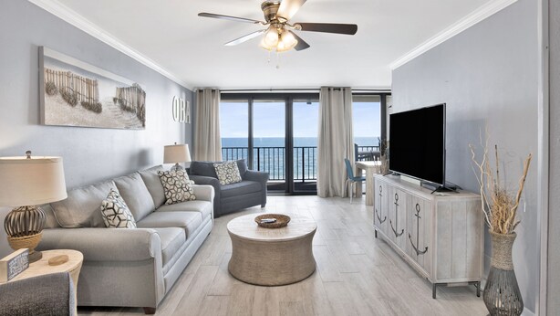 A modern living room with a grey sofa, a round coffee table, a TV on a white cabinet, and a ceiling fan. - Beachfront 1BR @ Phoenix I • Sleeps 6 • Stunning Views, Pool, Splash Pad & Beach Access (Orange Beach)