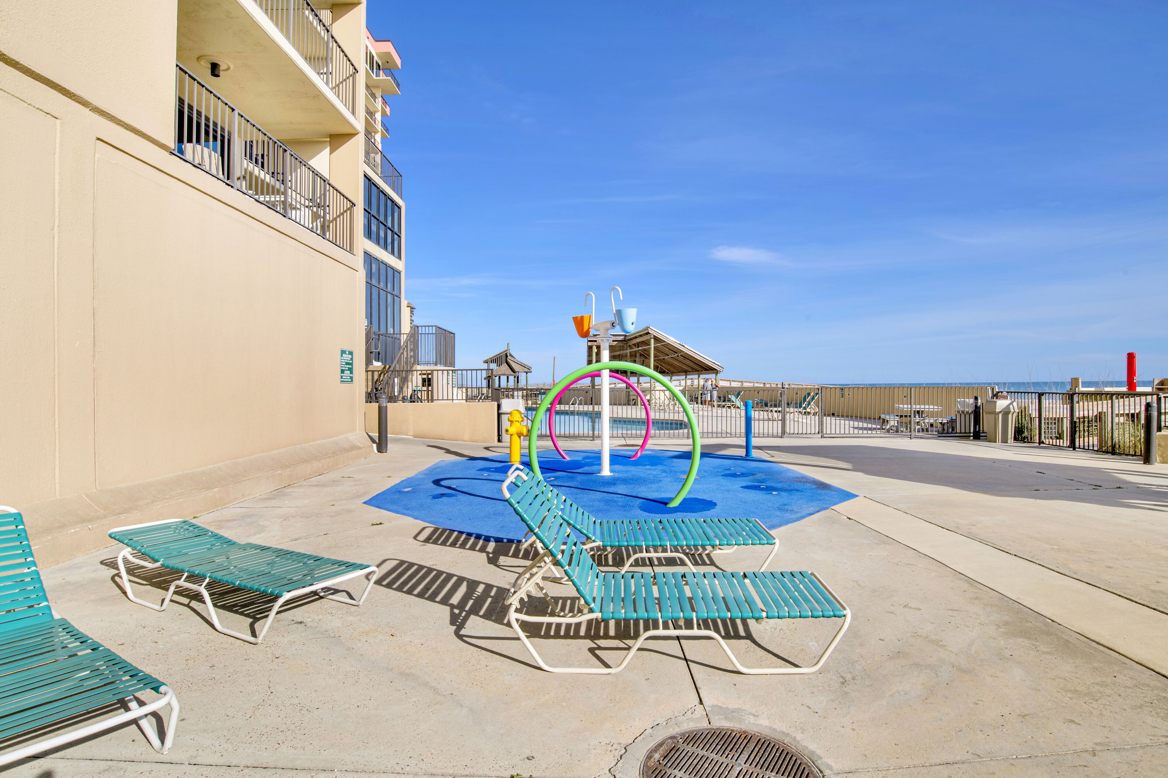 A poolside area with lounge chairs, a water play structure, and a building with balconies.