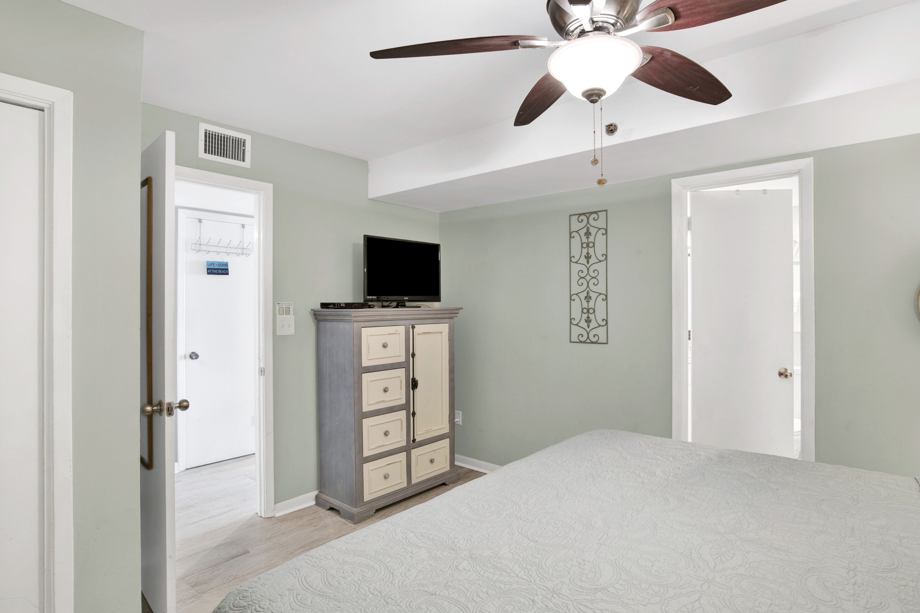 Une chambre à coucher avec un lit, un ventilateur de plafond, un téléviseur posé sur un meuble et une porte avec une pancarte.