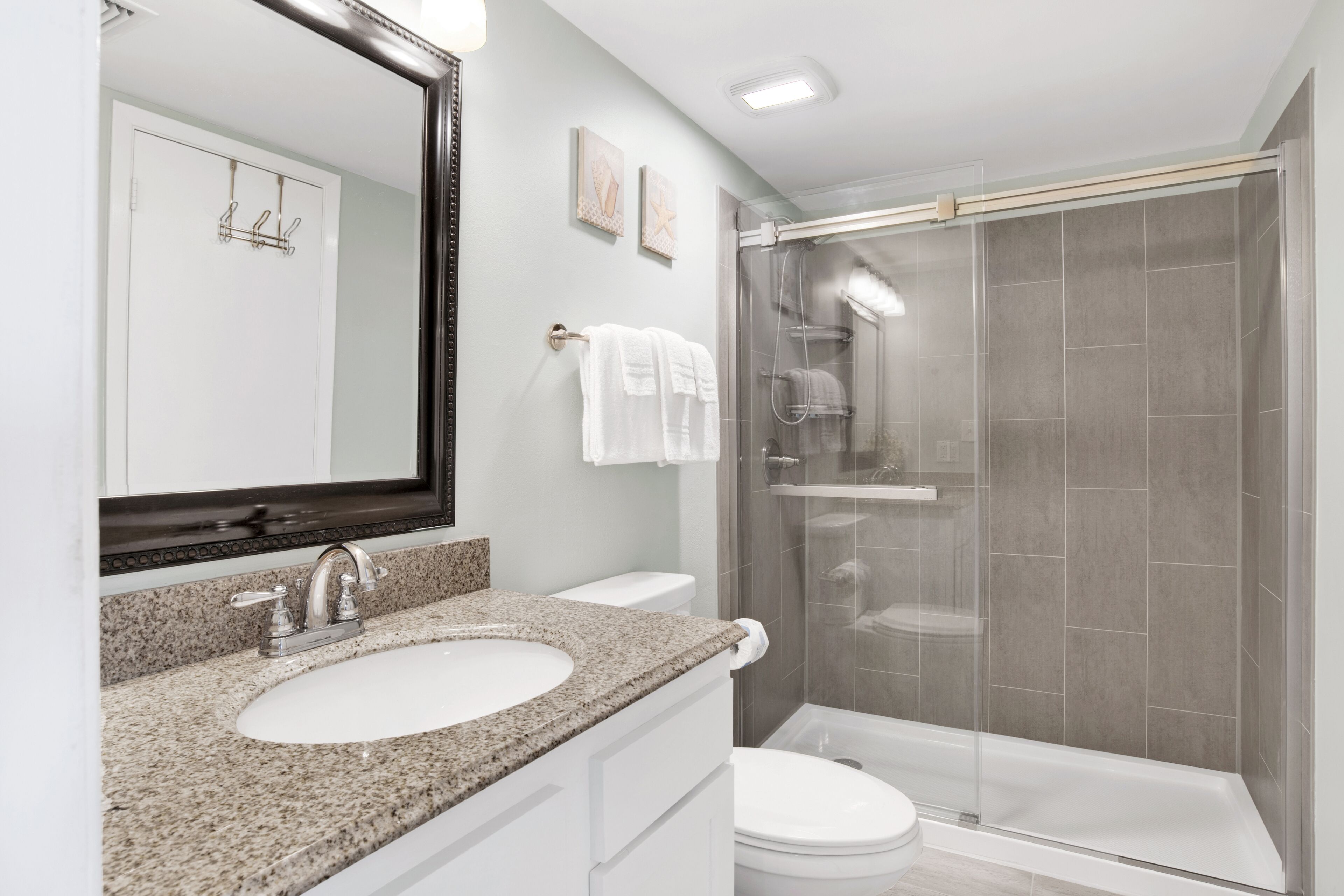 Une salle de bain moderne avec un lavabo surmonté d’un plan de travail en granit, des toilettes blanches et une douche à parois de verre.