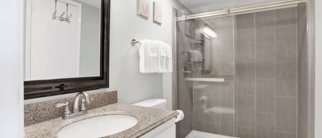 Une salle de bain moderne avec un lavabo surmonté d’un plan de travail en granit, des toilettes blanches et une douche à parois de verre.